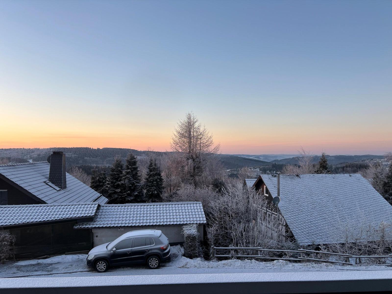 Schneebedeckte Dächer und Bäume bei Sonnenuntergang