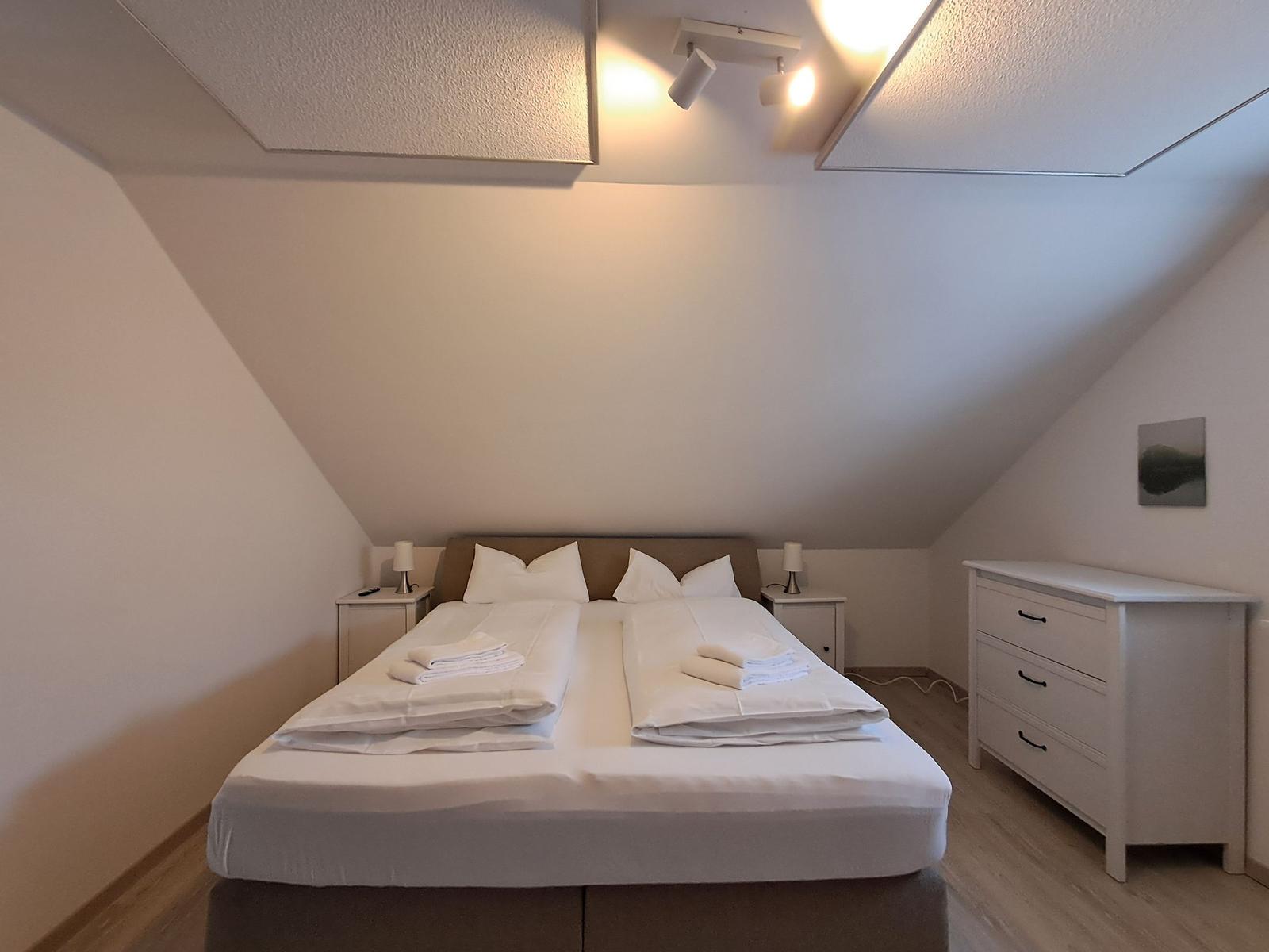 Schlafzimmer mit Doppelbett, Nachttischen und Schrank unter schrägen Dachdecken.