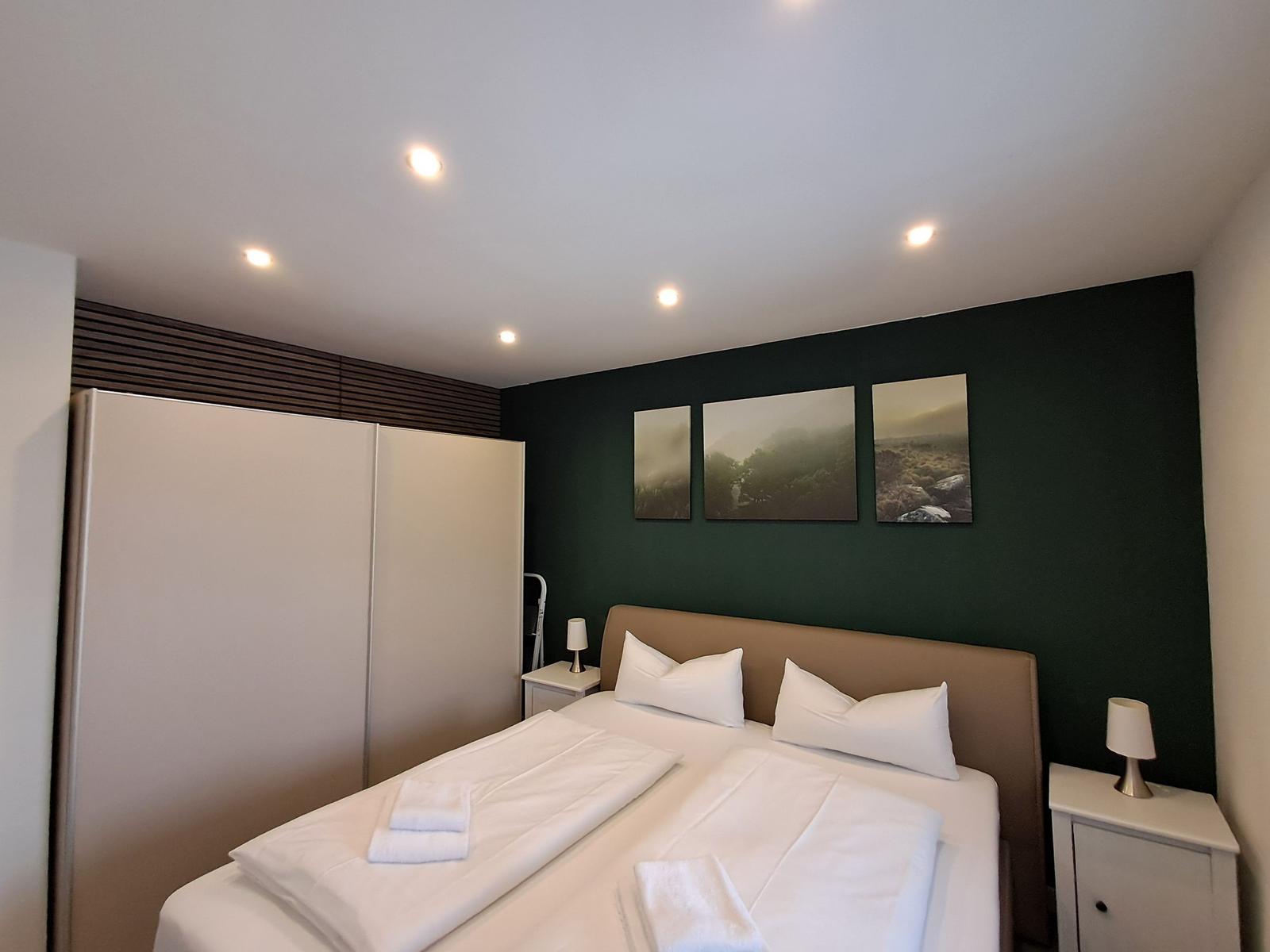 Schlafzimmer mit Bett, Nachttischen und Wandbildern.