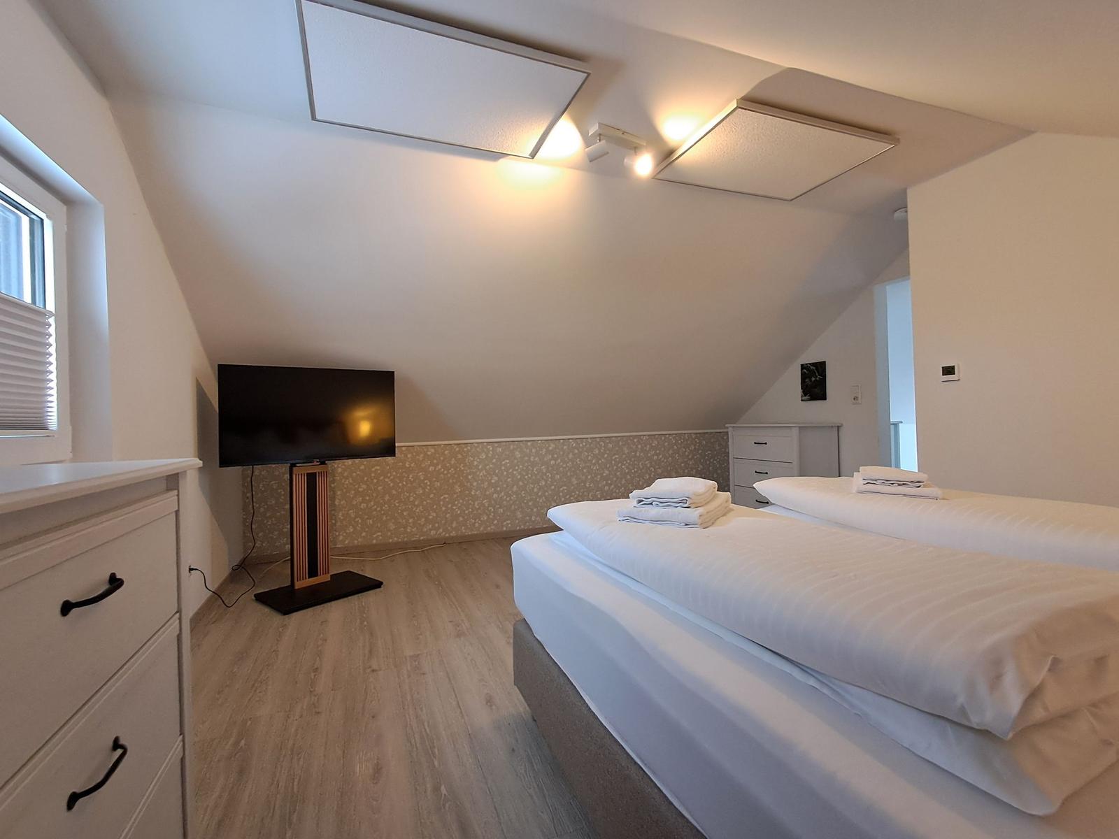 Schlafzimmer mit Doppelbett, TV und Schränken unter schrägem Dach