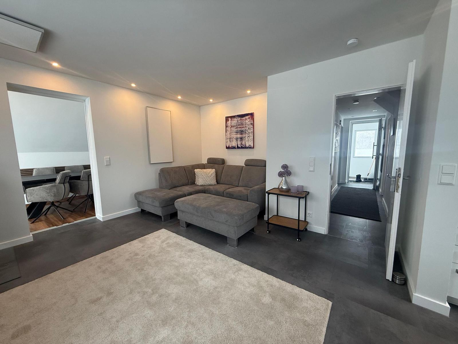 Wohnzimmer mit grauem Sofa, Teppich und Blick in Essbereich und Flur.