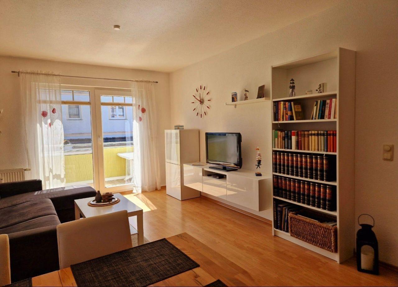 Wohnzimmer mit Sofa, Fernseher und Bücherregal. Durchgang zur Terrasse mit Tisch.