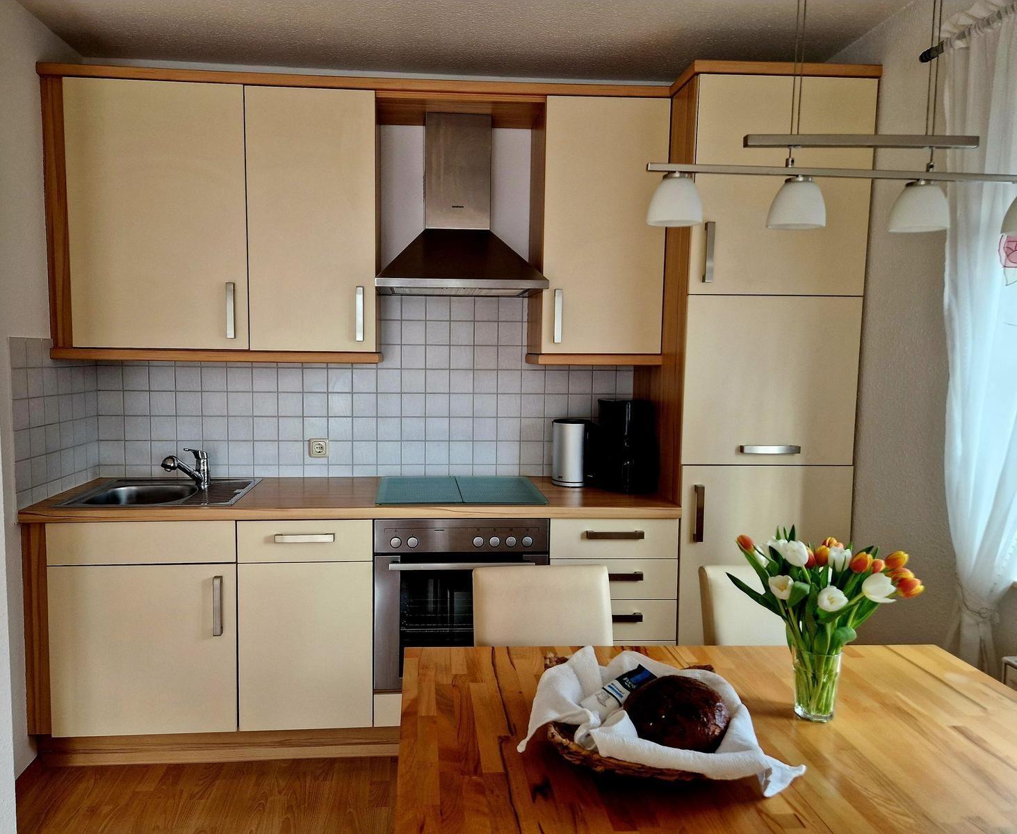 Küche mit Holzwerkstoffmöbeln, Edelstahlherd und Küchentisch mit Blumen.