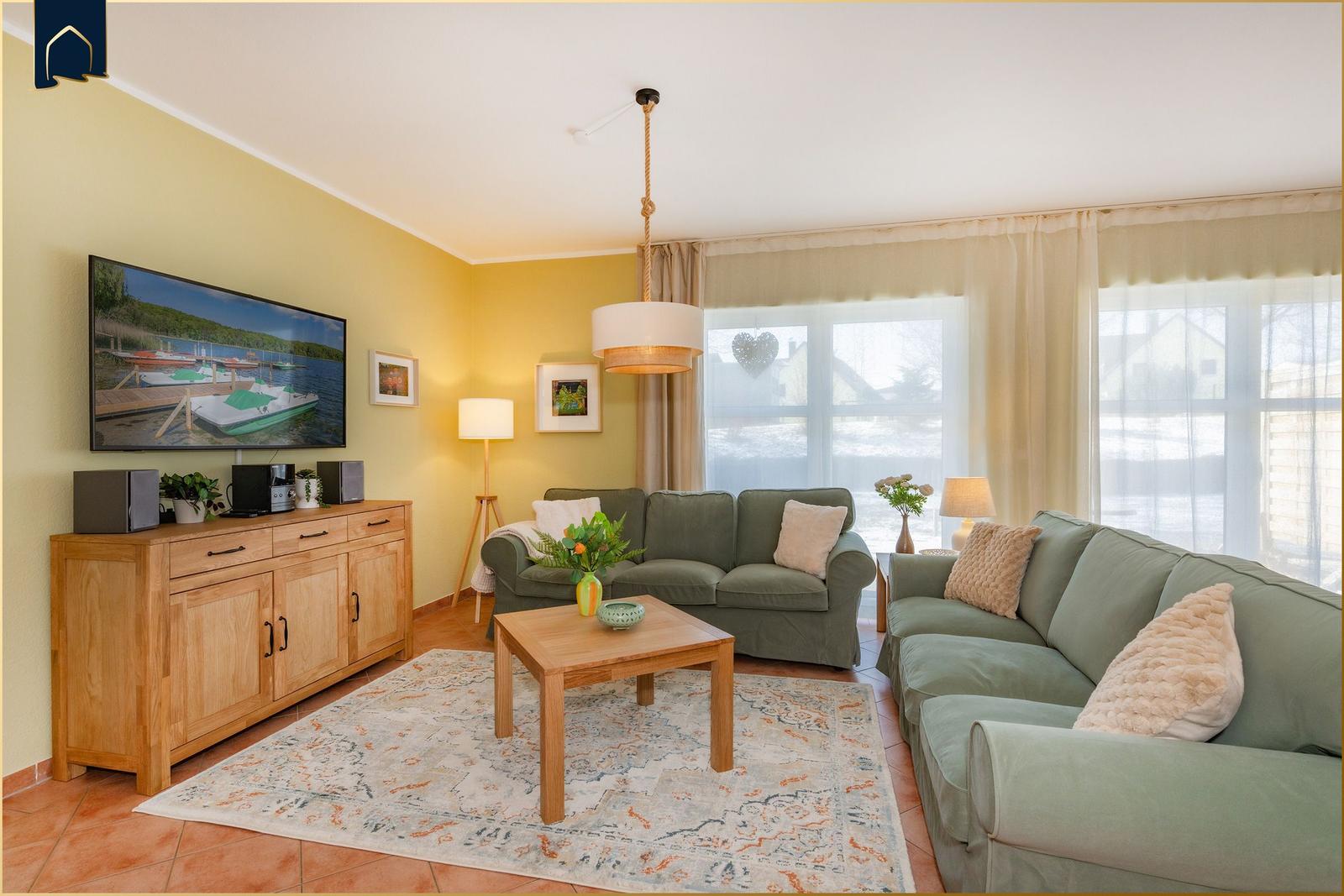 Wohnzimmer mit zwei Sofas, Couchtisch, Fernseher und großen Fenstern.