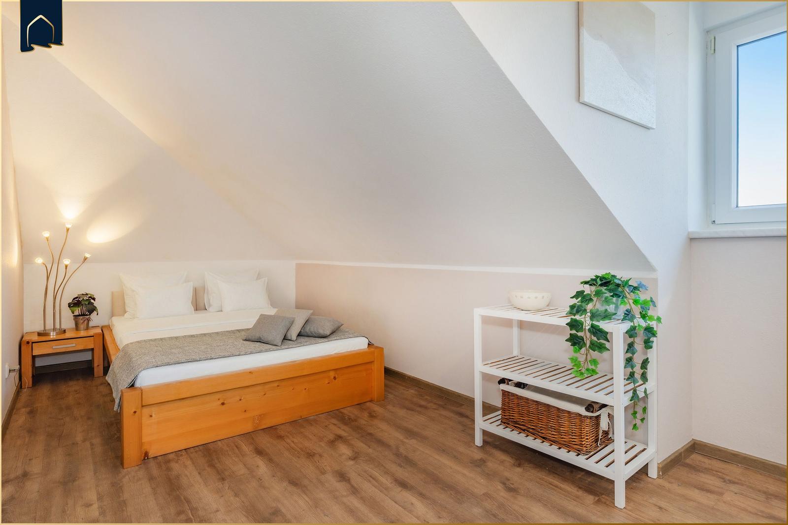Schlafzimmer mit Dachschräge, Holzbett, Nachttisch und Pflanzen.