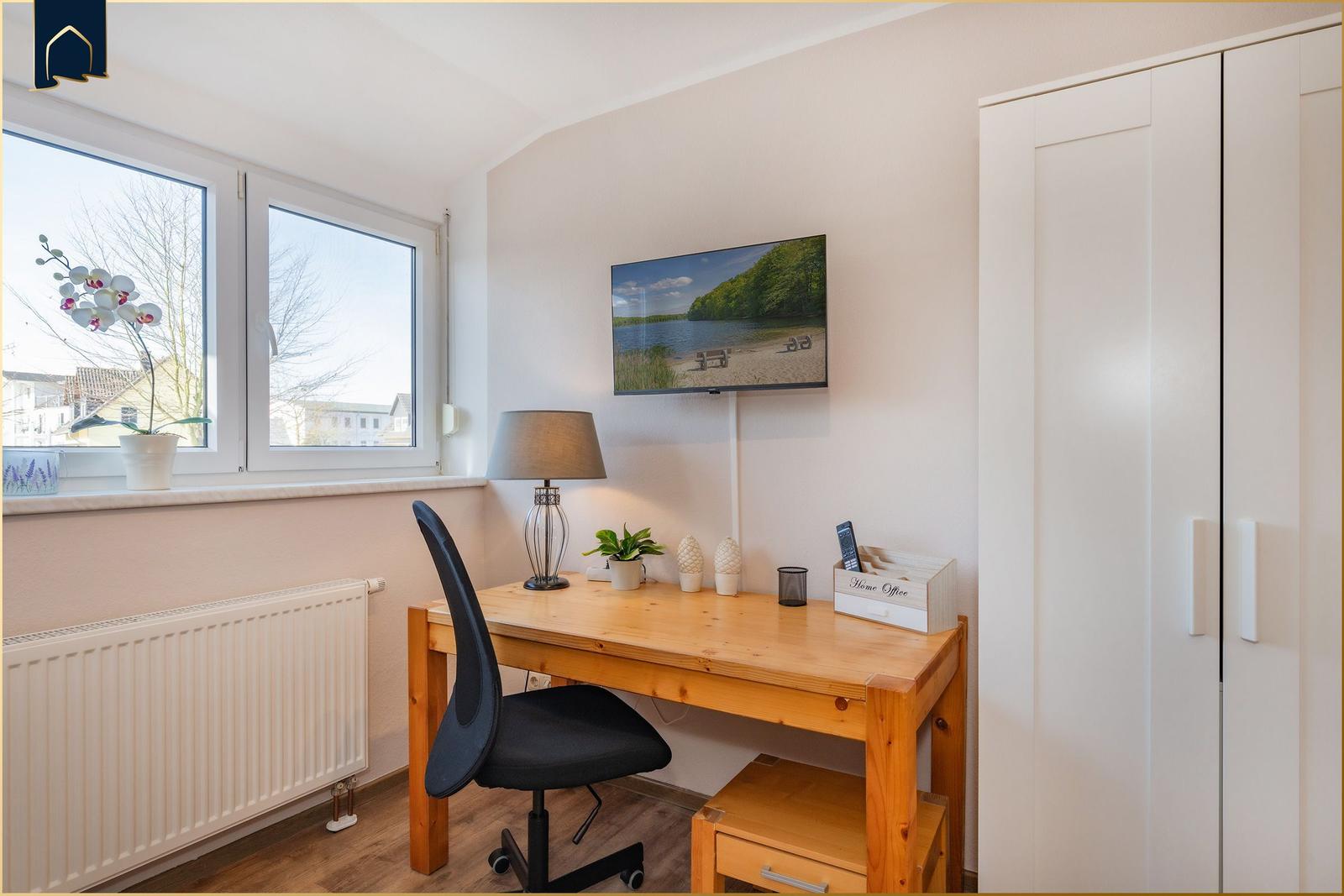 Arbeitszimmer mit Schreibtisch, Stuhl und Fernseher an der Wand.