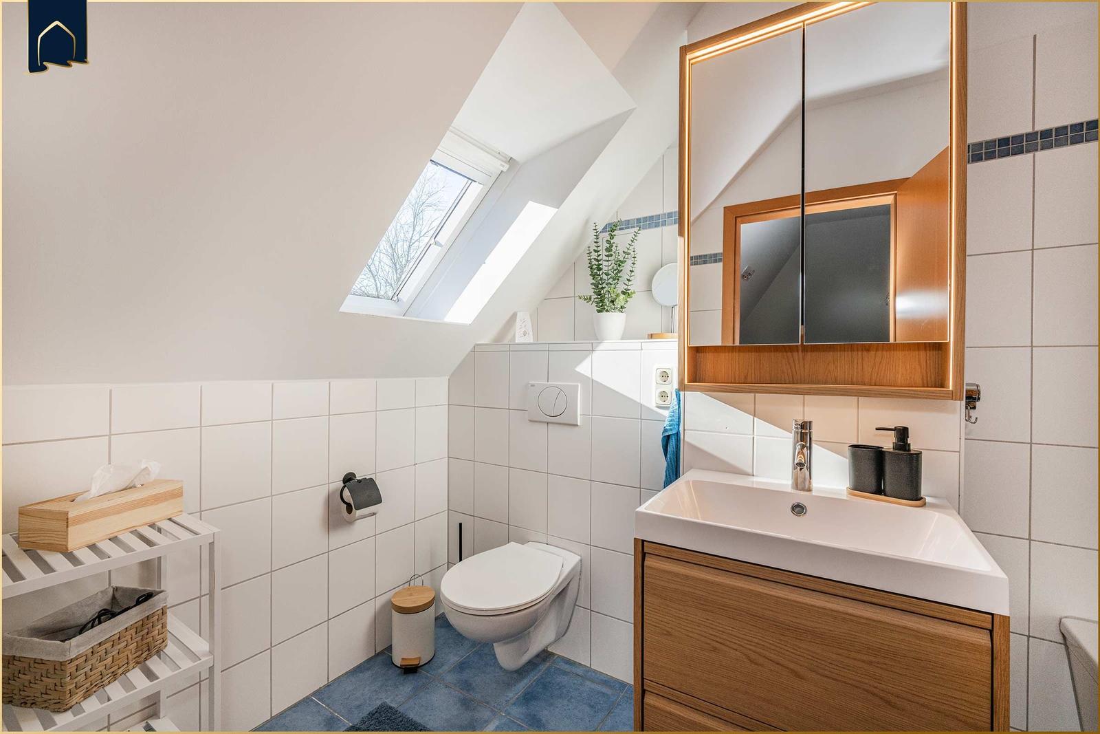 Badezimmer mit Dachschräge, Waschbecken, Spiegel und Toilette.
