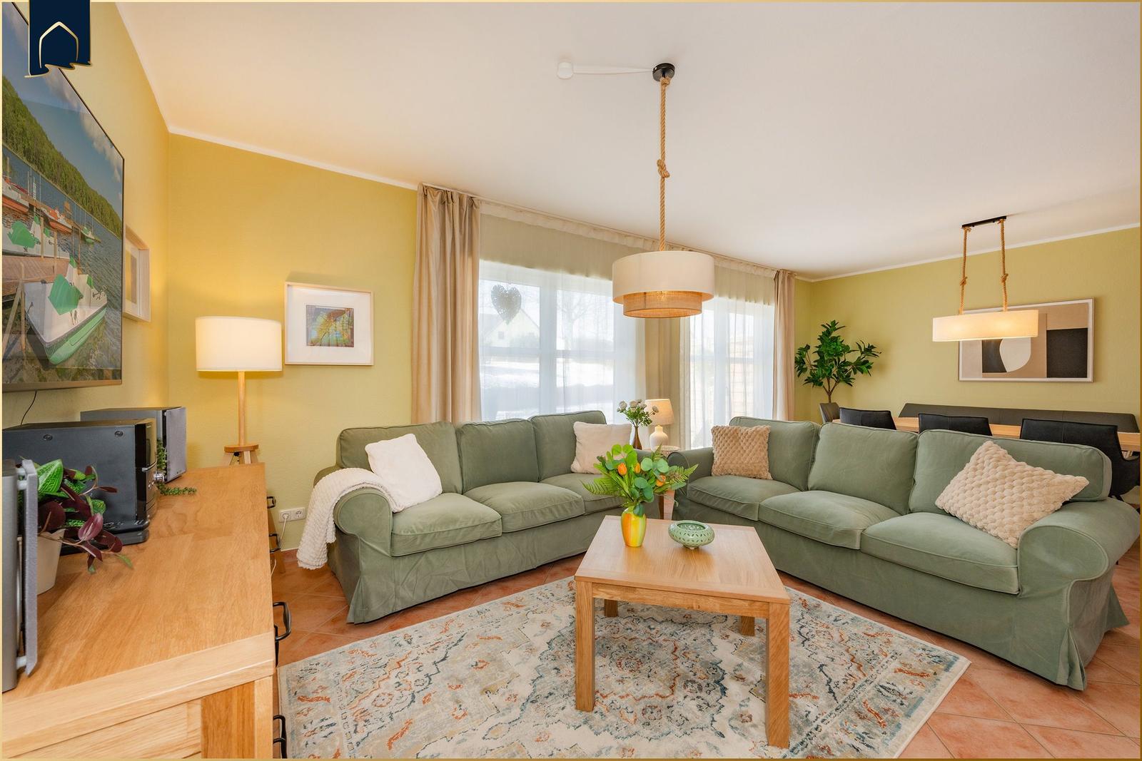 Wohnzimmer mit grünem Sofa, Holztisch und Fernseher.