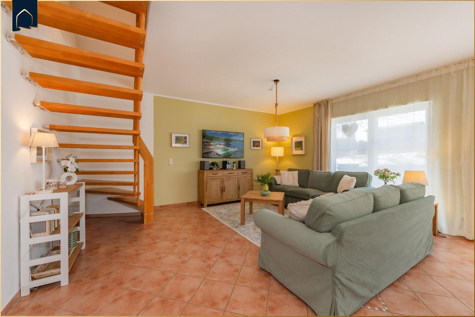 Wohnzimmer mit Sofa, Fernseher und Holztreppe.