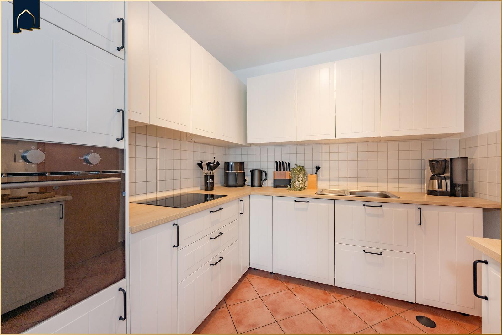 Küche mit weißen Schränken, Holzoberflächen und integriertem Backofen.