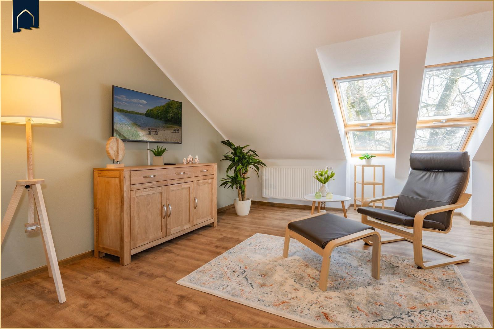 Wohnzimmer mit Sessel, Fernseher und Holzmöbeln unter Dachschrägen.