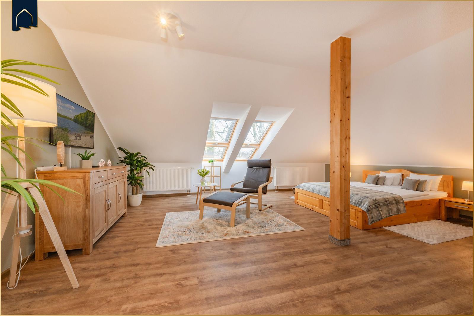 Schlafzimmer mit Dachschrägen, Bett, Sessel und Holzboden.