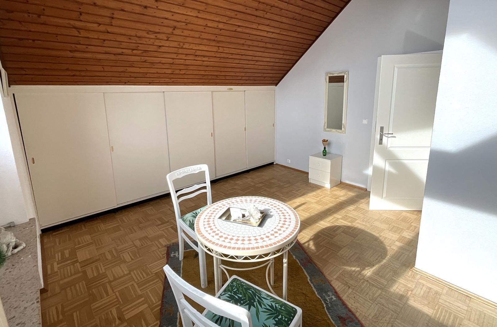 Raum mit Holzdecke, weißen Schränken, Tisch und Stühlen auf Parkettboden.