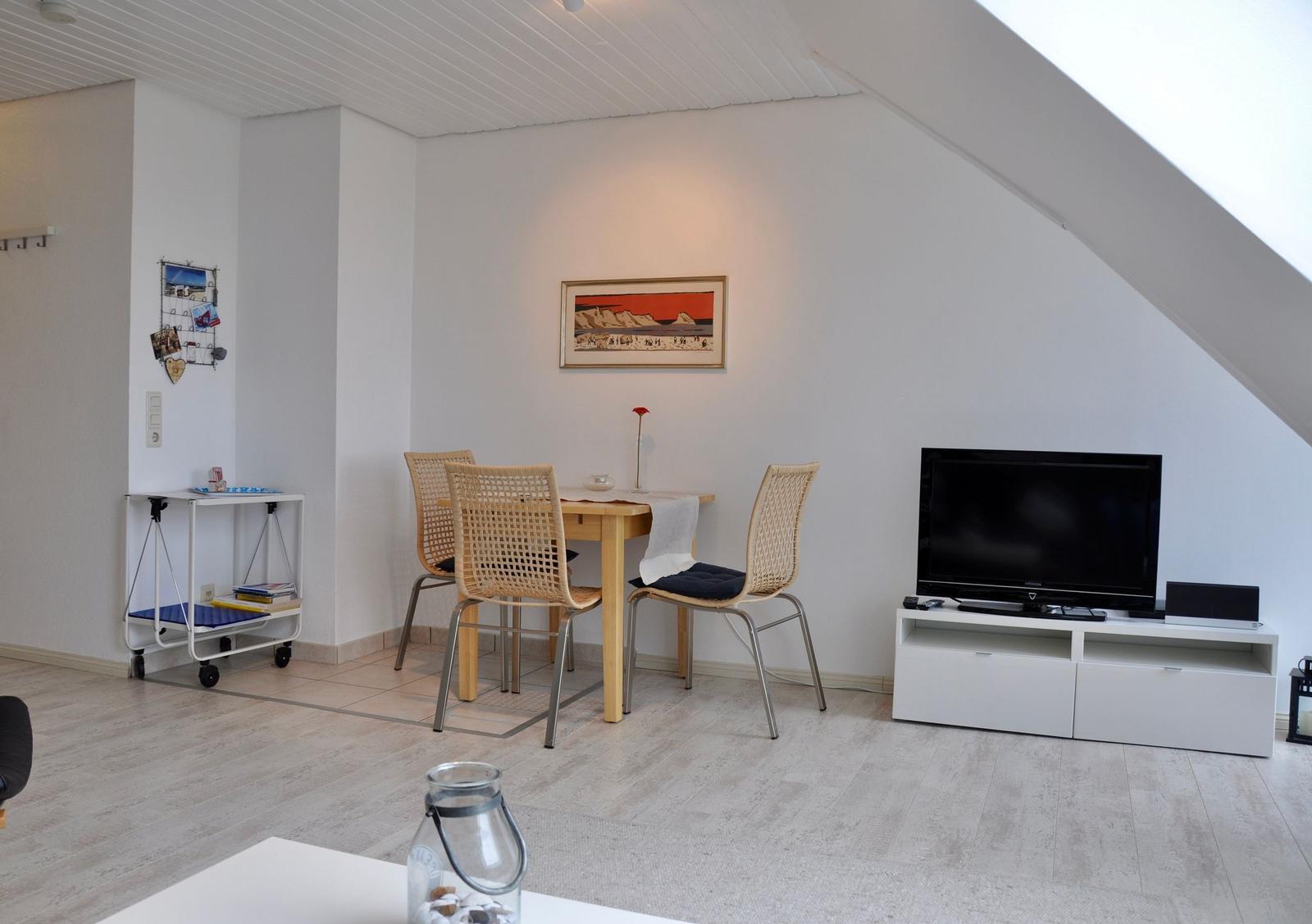 Wohn- und Essbereich mit TV, Tisch und Stühlen unter schrägem Dach