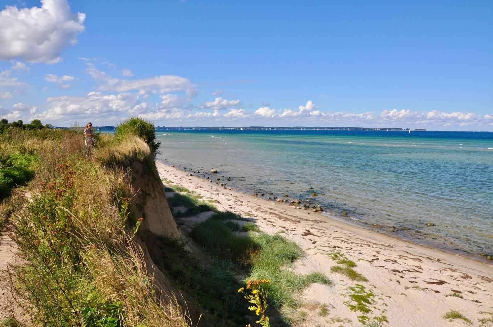 Strand mit Klippe und klarer See unter blauem Himmel mit Wolken.