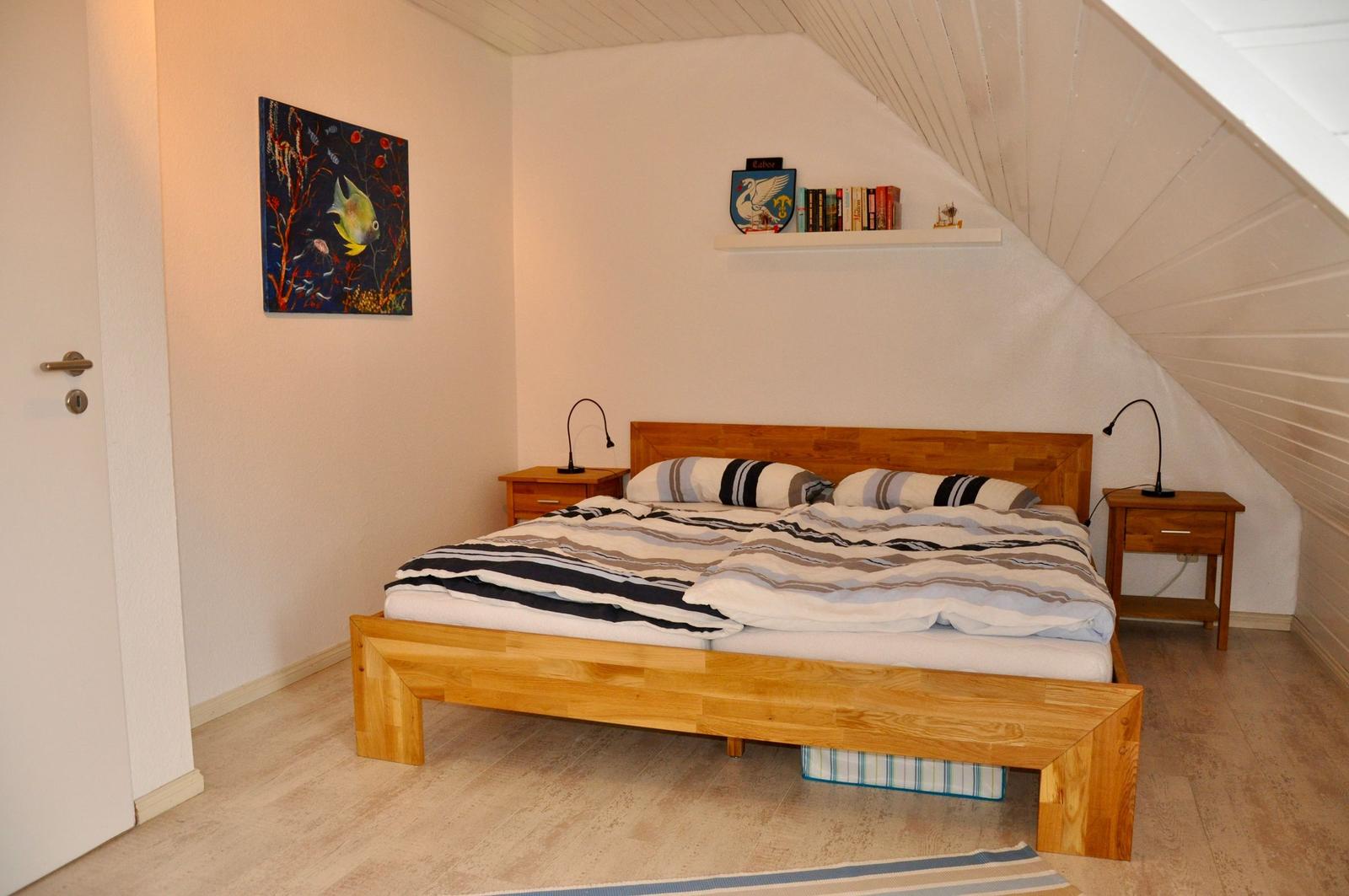 Schlafzimmer mit Dachschrägen, Holzbett und Nachttischen mit Lampen.