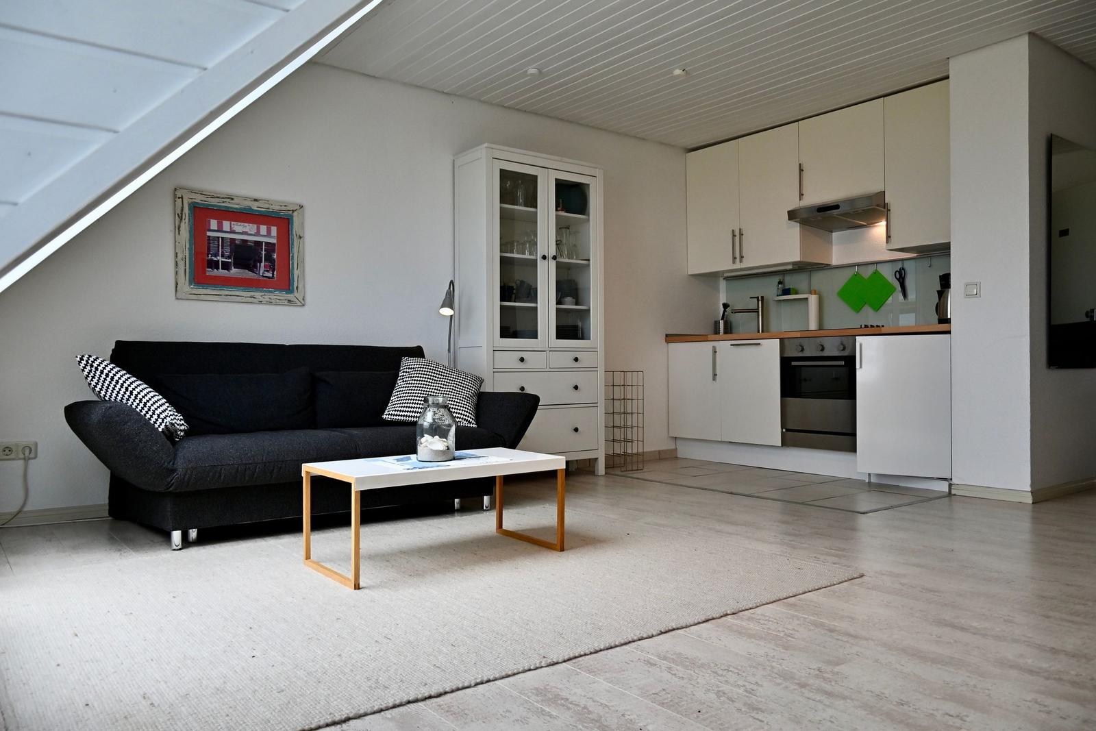 Wohnbereich mit Sofa, Couchtisch und Küche unter Dachschrägen.