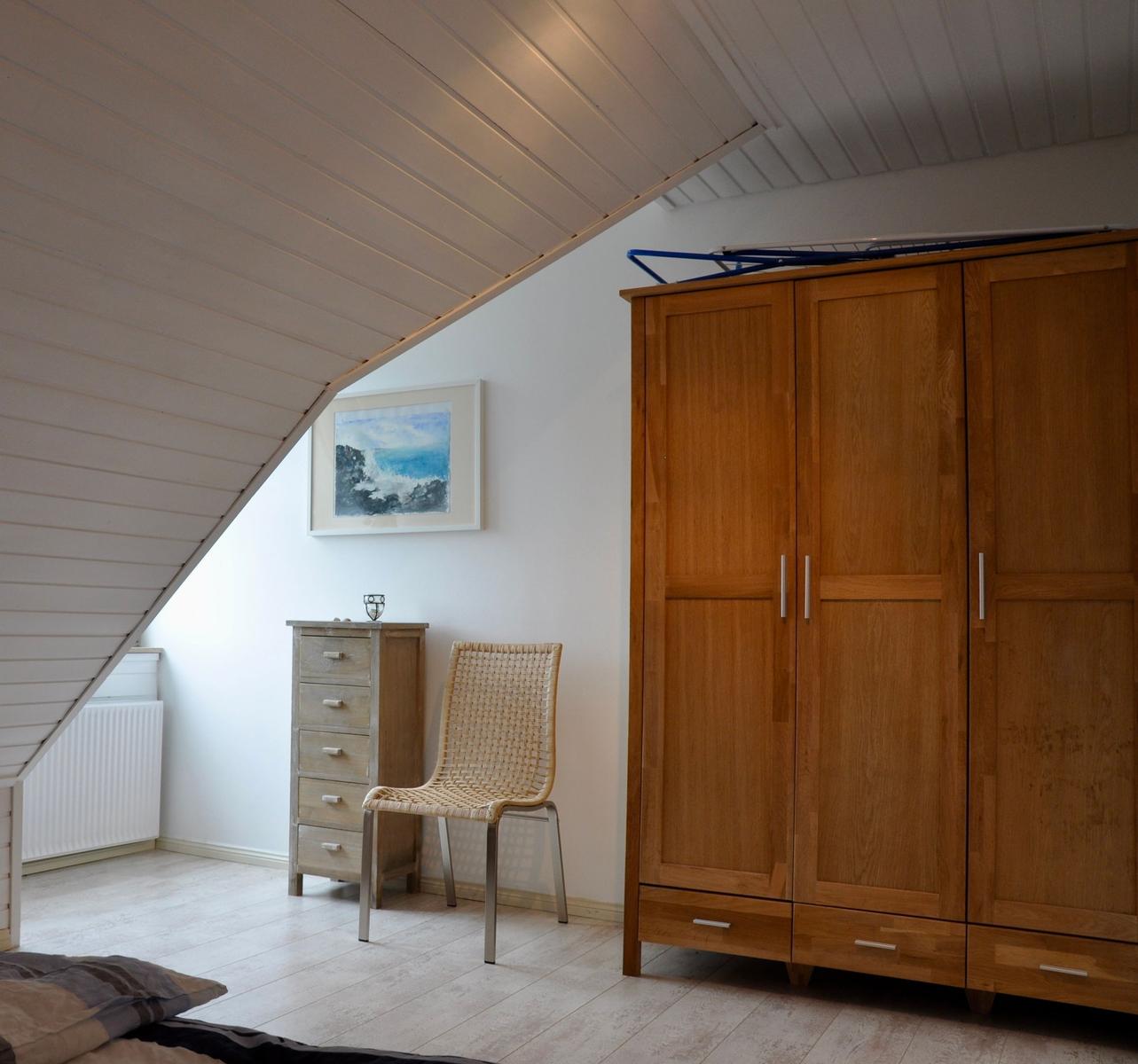 Schlafzimmer mit Holzschrank, Stuhl und Bild an der Wand unter schrägem Dach.