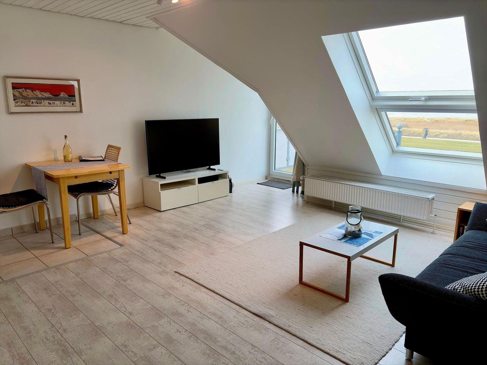 Wohnraum mit TV, Schreibtisch und Dachfenster mit Blick auf Grünfläche.