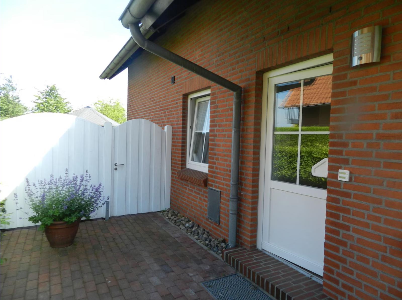 Rotes Backsteinhaus mit weißer Tür und Pflanze im Vorgarten.