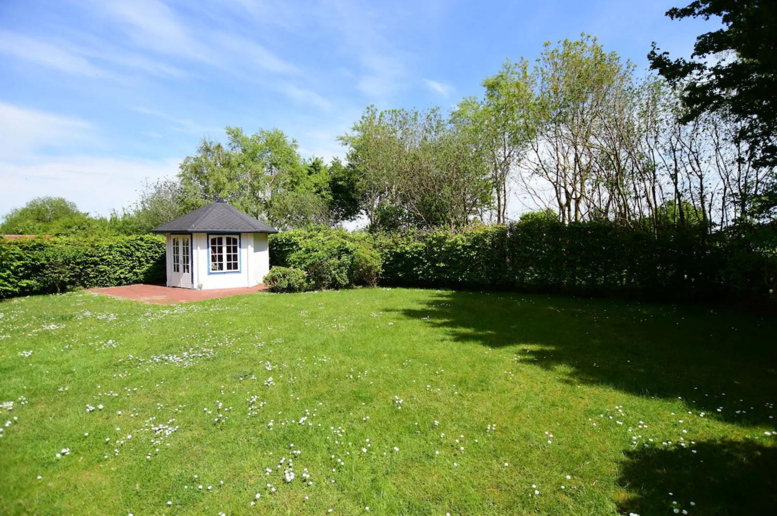 Ein weißer Pavillon mit dunklem Dach steht auf einer grünen Wiese mit weißen Blumen.