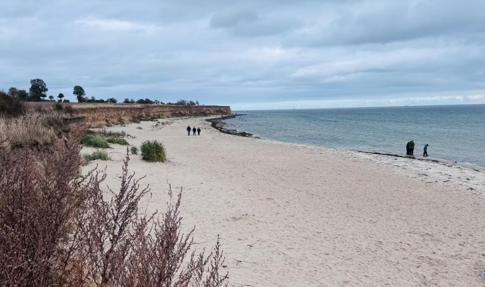 Strand mit Sand, Felsen und wenigen Personen am Wasser.