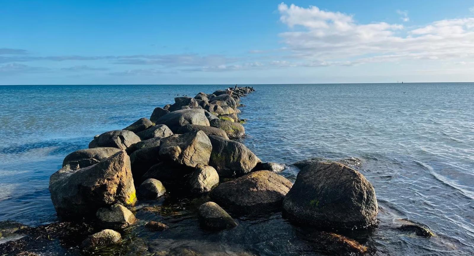 Steinreihe führt ins Meer unter blauem Himmel