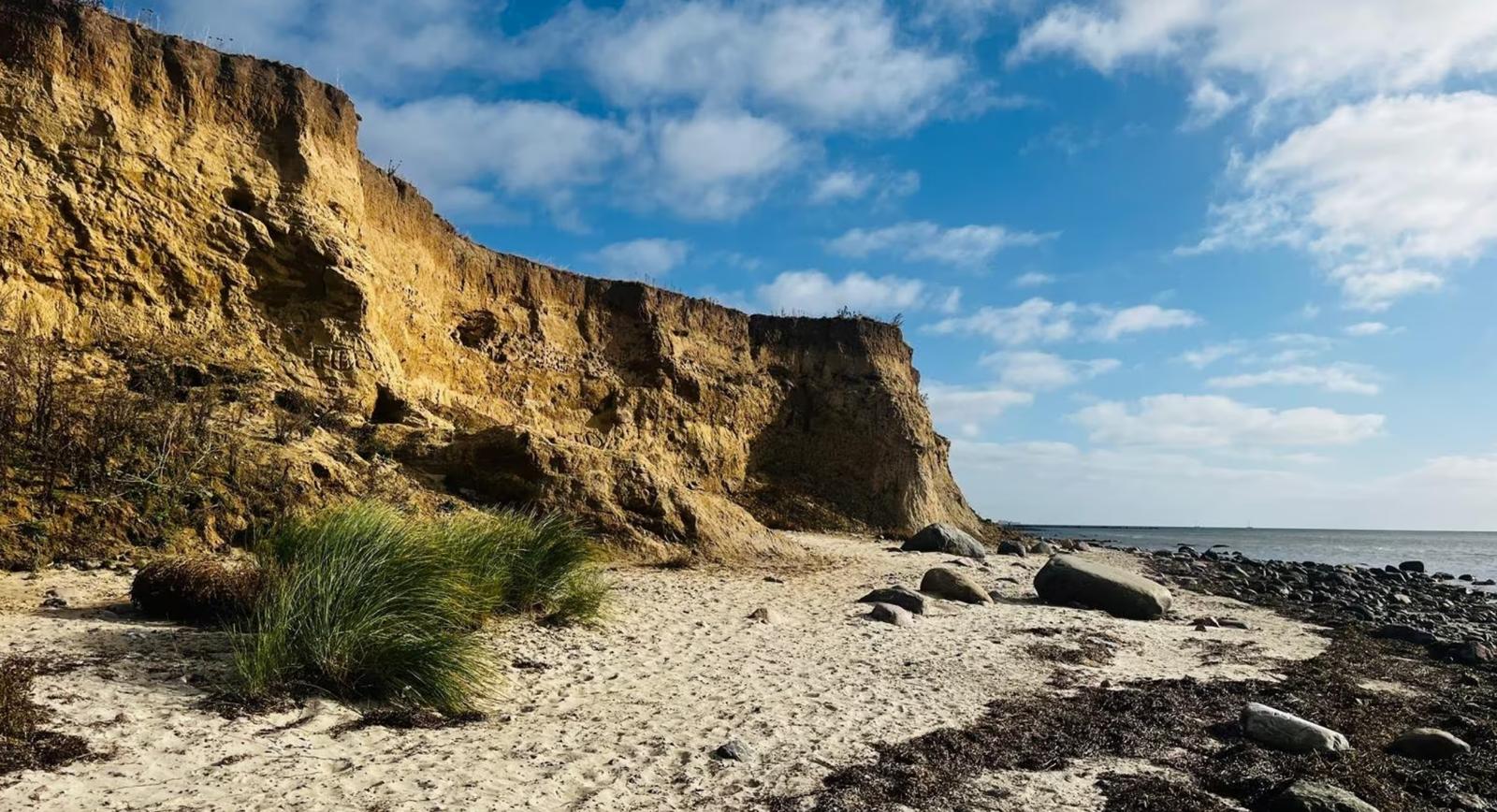 Steilküste mit Strand und Felsen unter blauem Himmel.