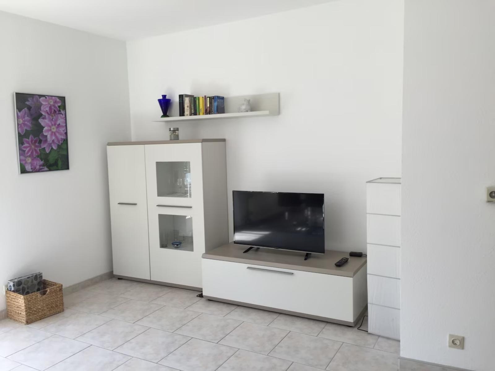 Wohnzimmer mit TV, Sideboard und Wandregal. Wandbild und Korb sind sichtbar.