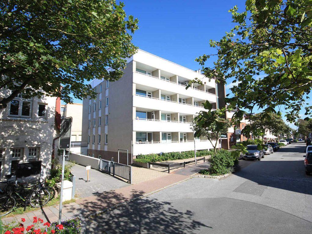 Wohnhaus mit Balkonen, umgeben von Bäumen und gepflasterten Wegen.