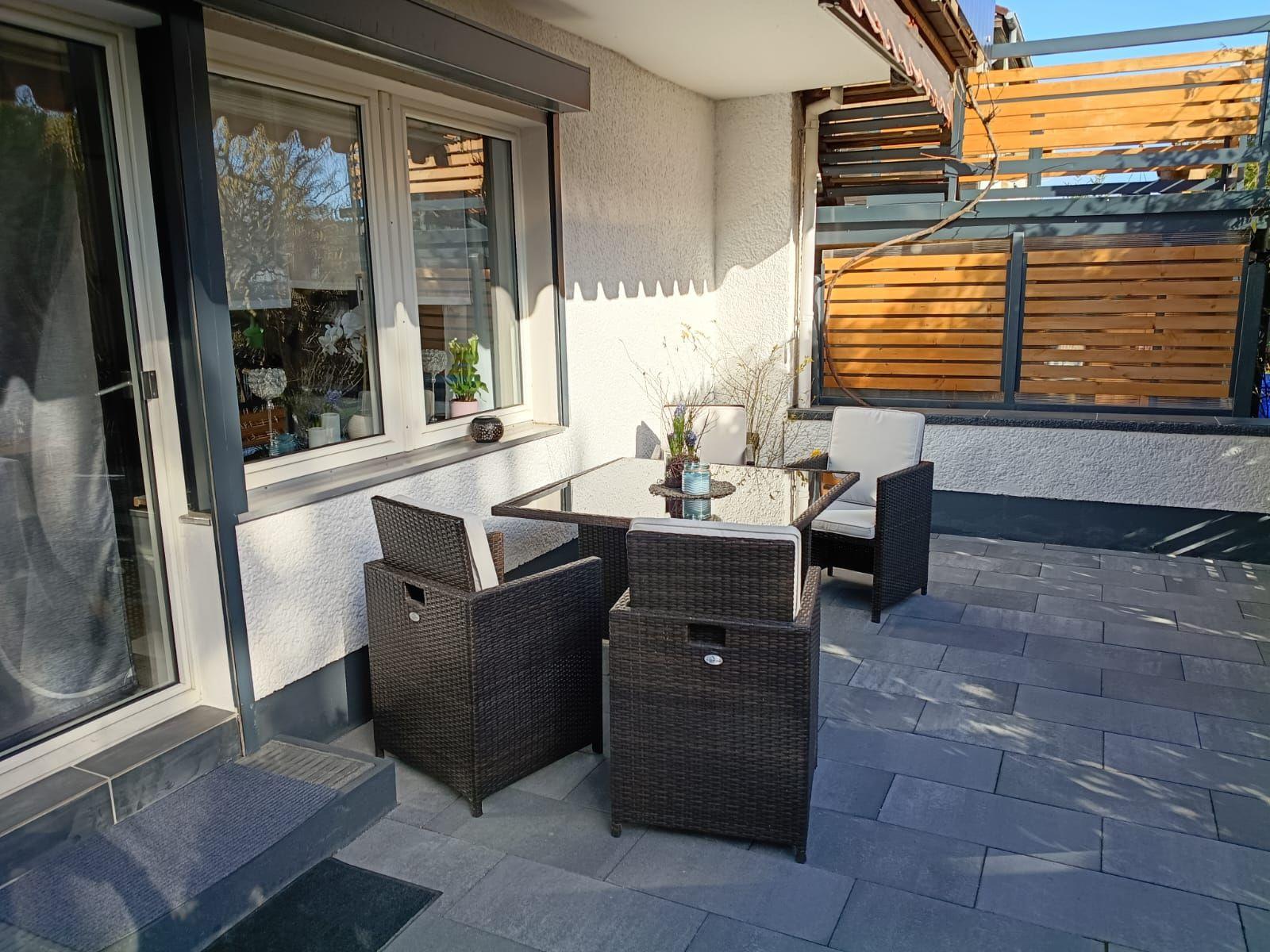 Terrasse mit Sitzgruppe und Holzverkleidung. Fliesenboden und Glasfront.