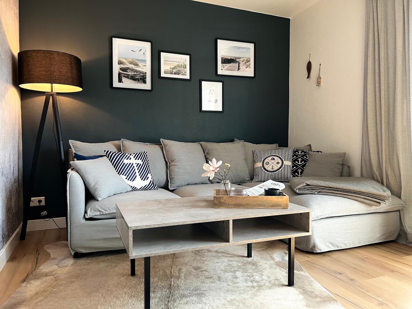 Ein Wohnzimmer mit grauem Sofa, Holztisch und dunkler Wand