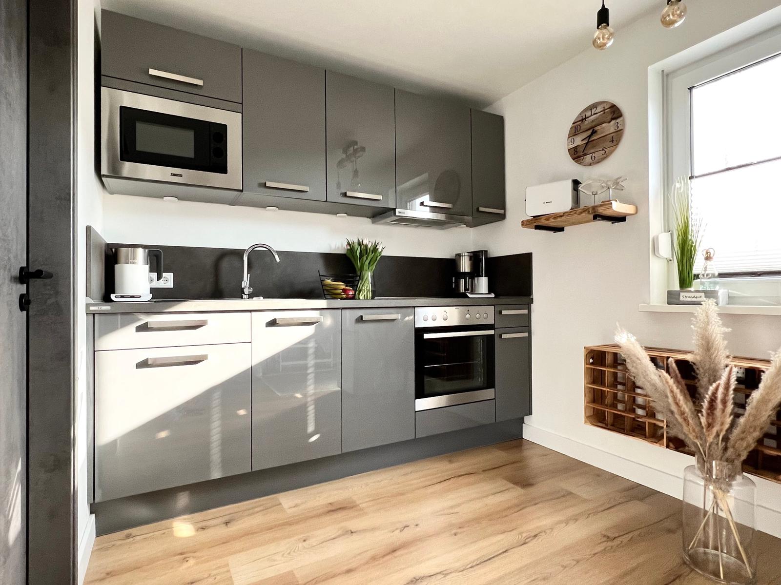 Moderne Küche mit grauen Schränken, Edelstahlgeräten und Holzboden.