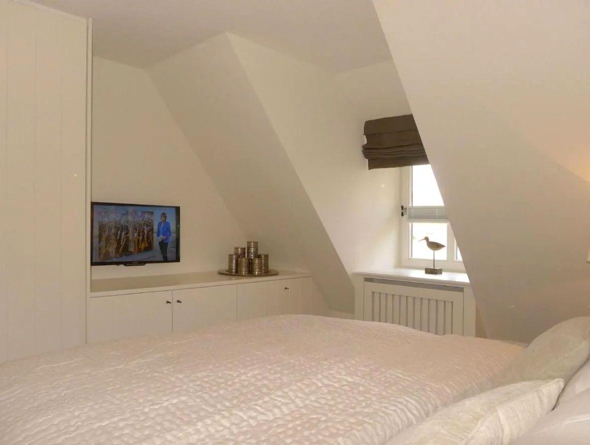 Schlafzimmer mit Dachschrägen, Bett, Fernseher und Fenster mit Vogeldekor.