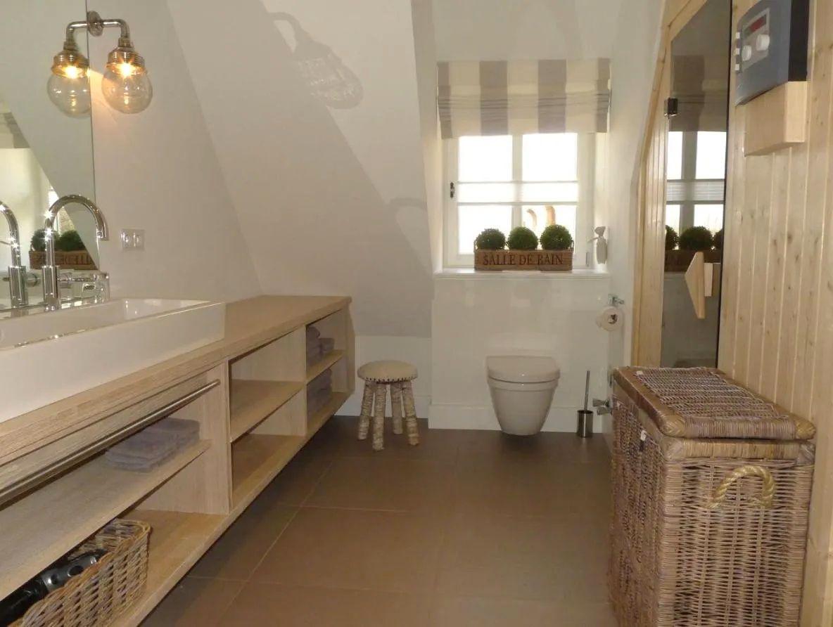 Badezimmer mit Waschbecken, Toilette und Dusche. Holzregal, Spiegel und Fenster mit Vorhang.