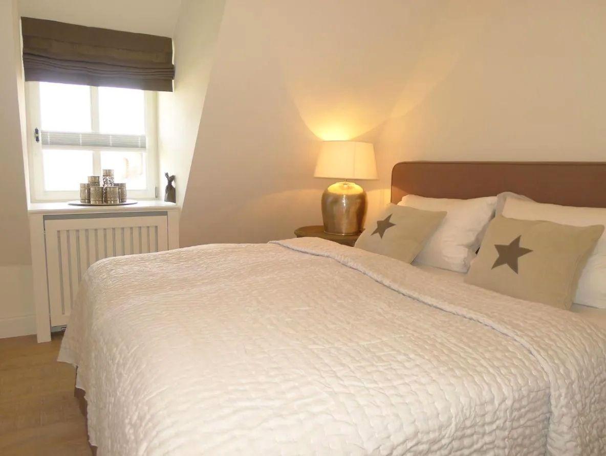 Schlafzimmer mit Bett, Nachttisch, Lampe und Fenster.