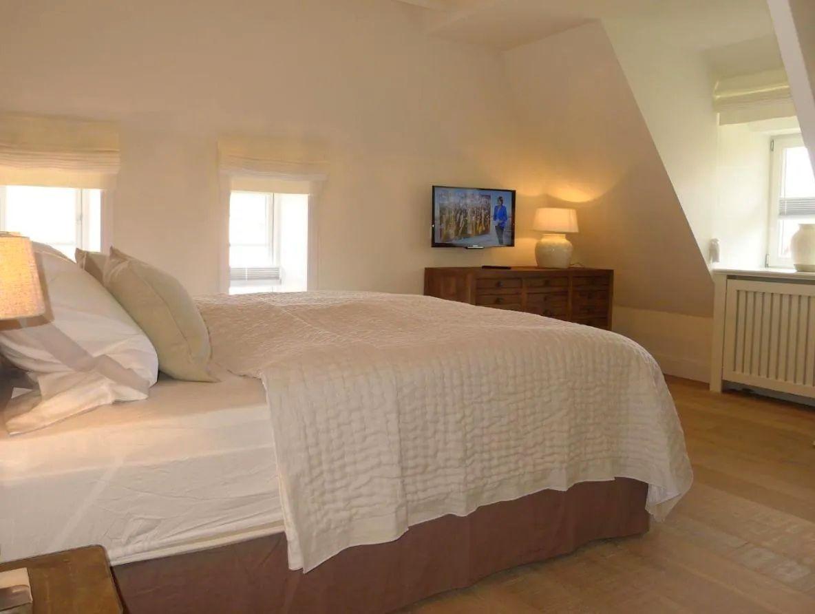 Schlafzimmer mit Bett, Fernseher und Fenstern.