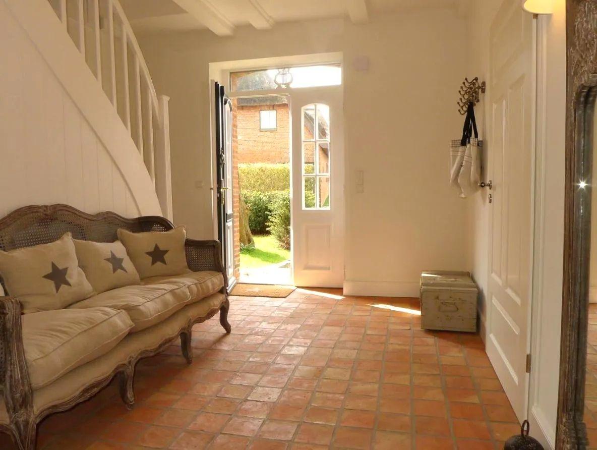 Eingangsbereich mit Sofa, Terrakottaboden und offenem Durchgang zur Außenterrasse.