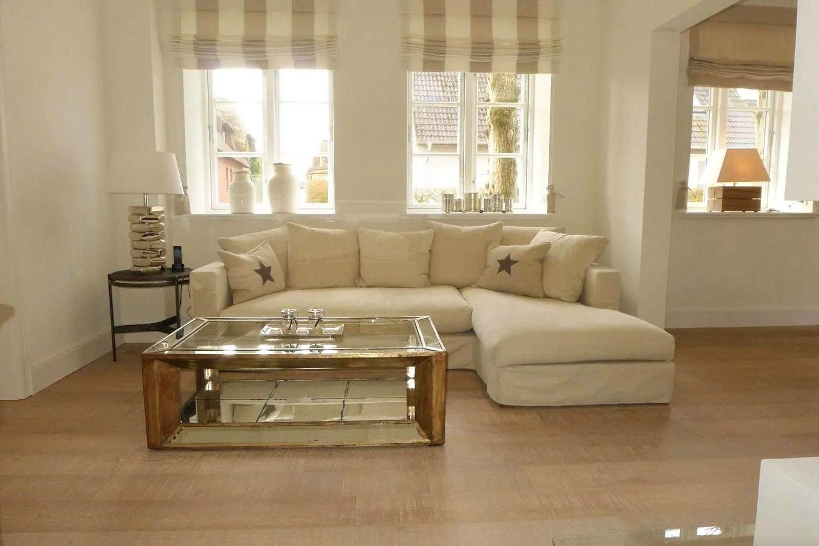 Wohnzimmer mit L-förmigem Sofa, Glas-Tisch und Fenstern mit Rollläden.