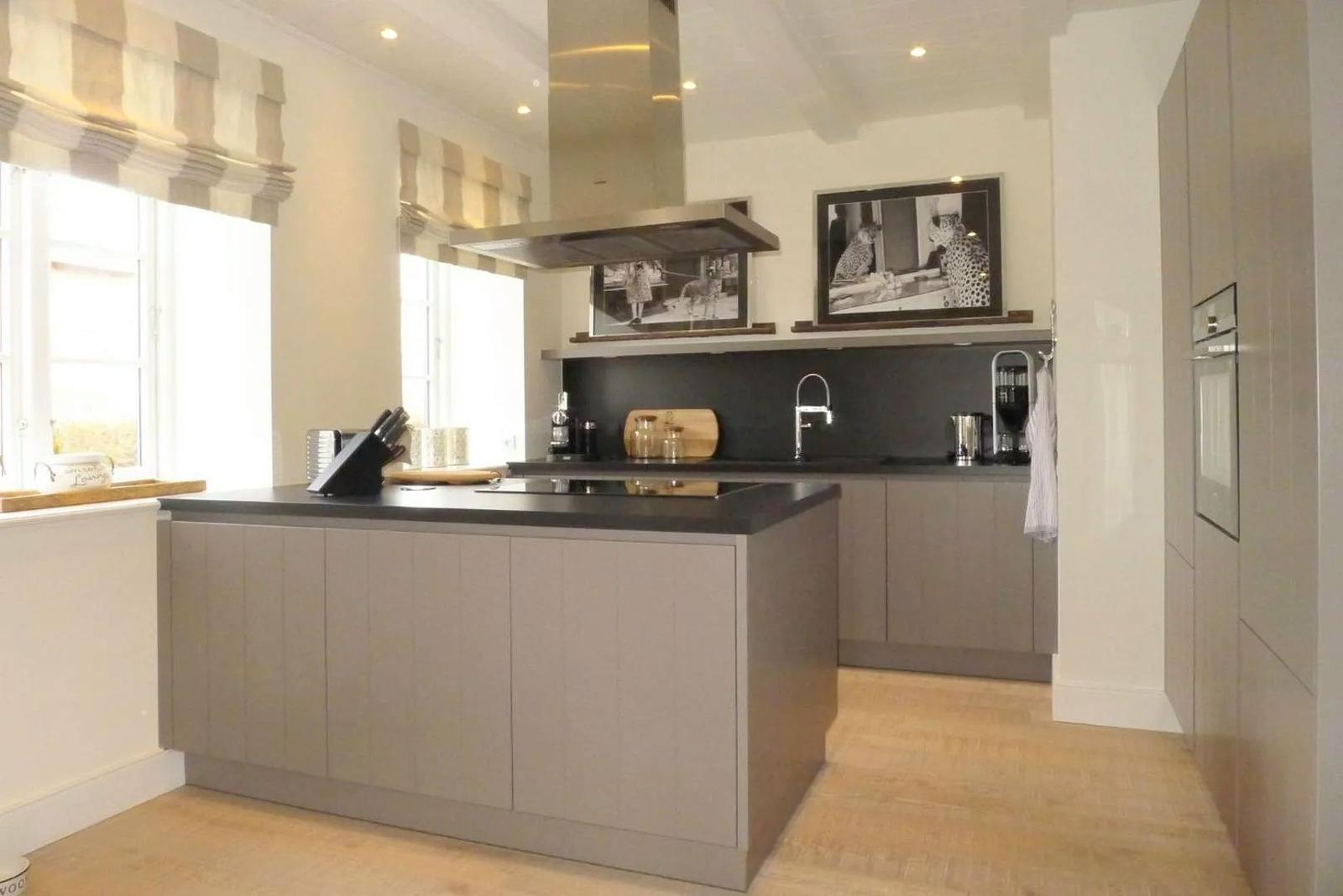 Moderne Küche mit Kücheninsel, dunkler Arbeitsplatte und Fenstern mit Raffstoren.