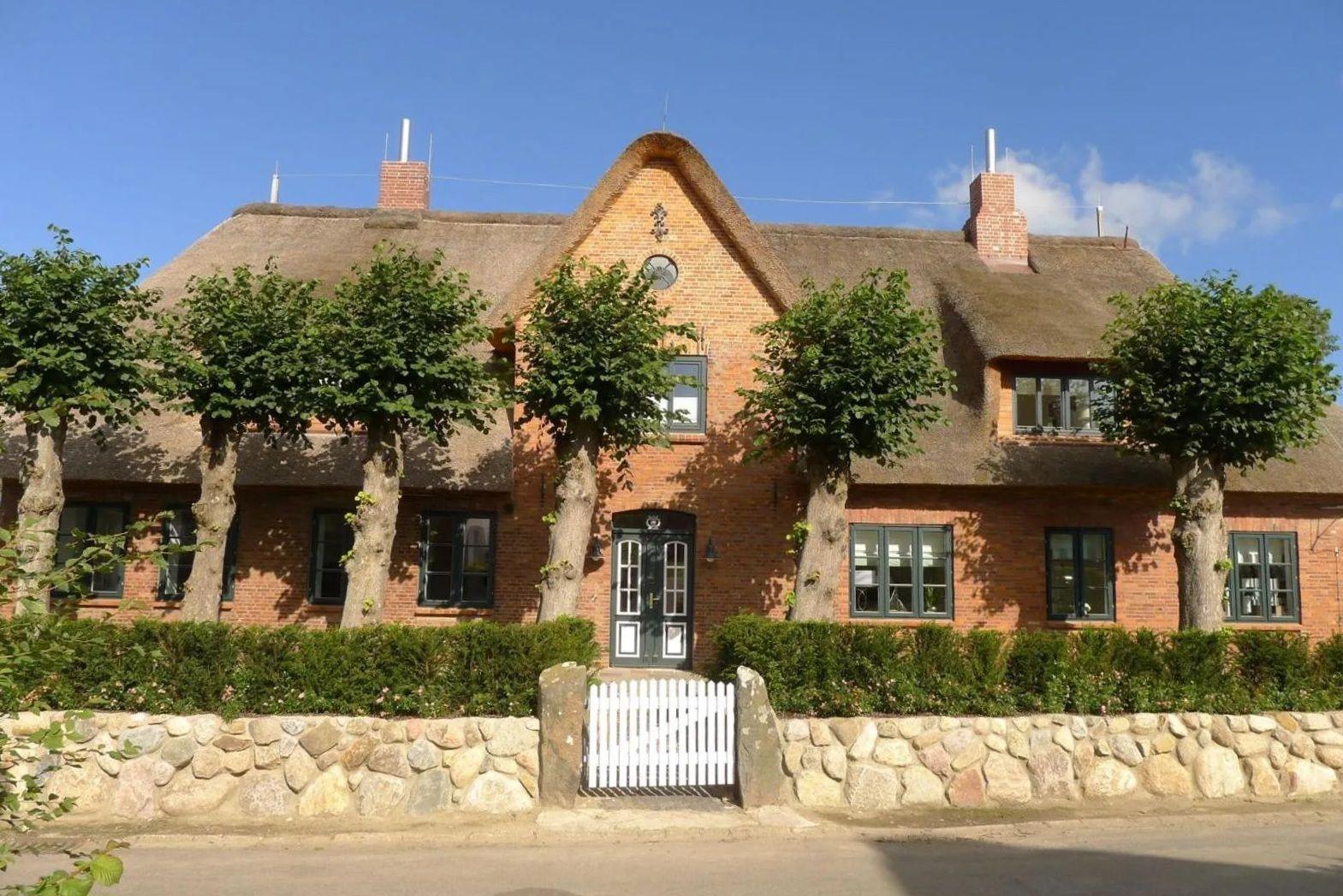 Rotes Backsteinhaus mit Strohdach, grünen Bäumen und weißem Tor