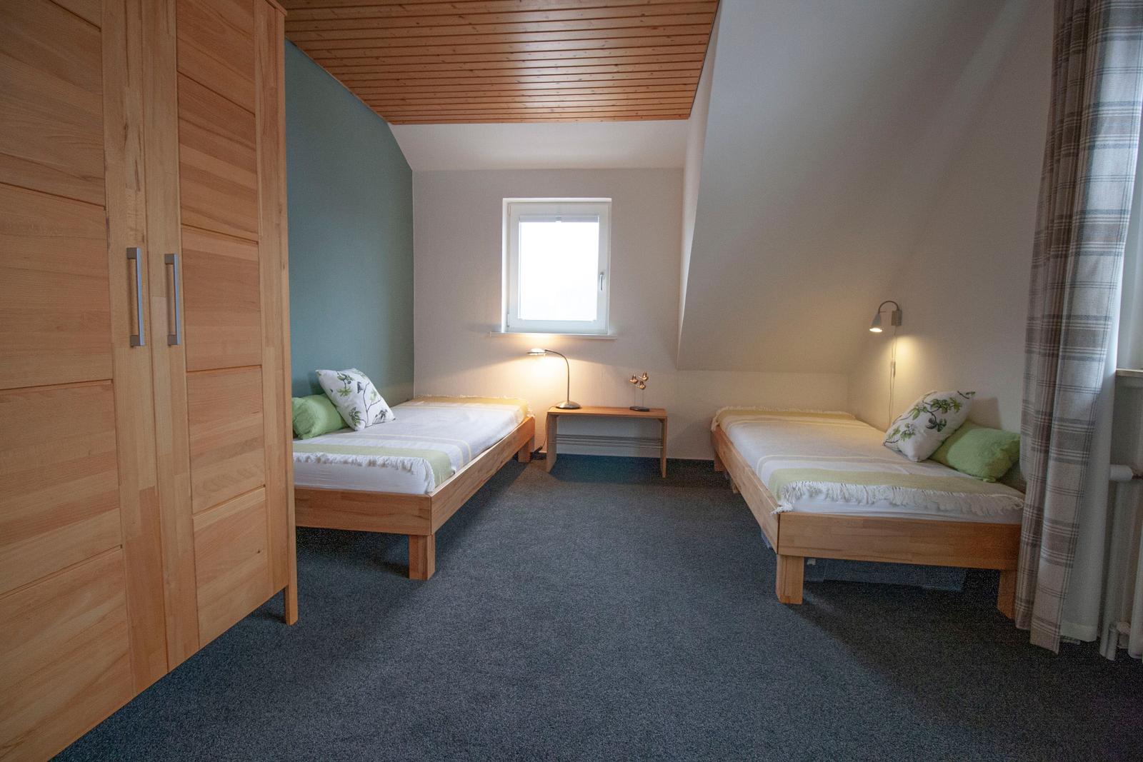 Zwei Einzelbetten, Kleiderschrank, Fenster und Wandlampen in einem Schlafzimmer.