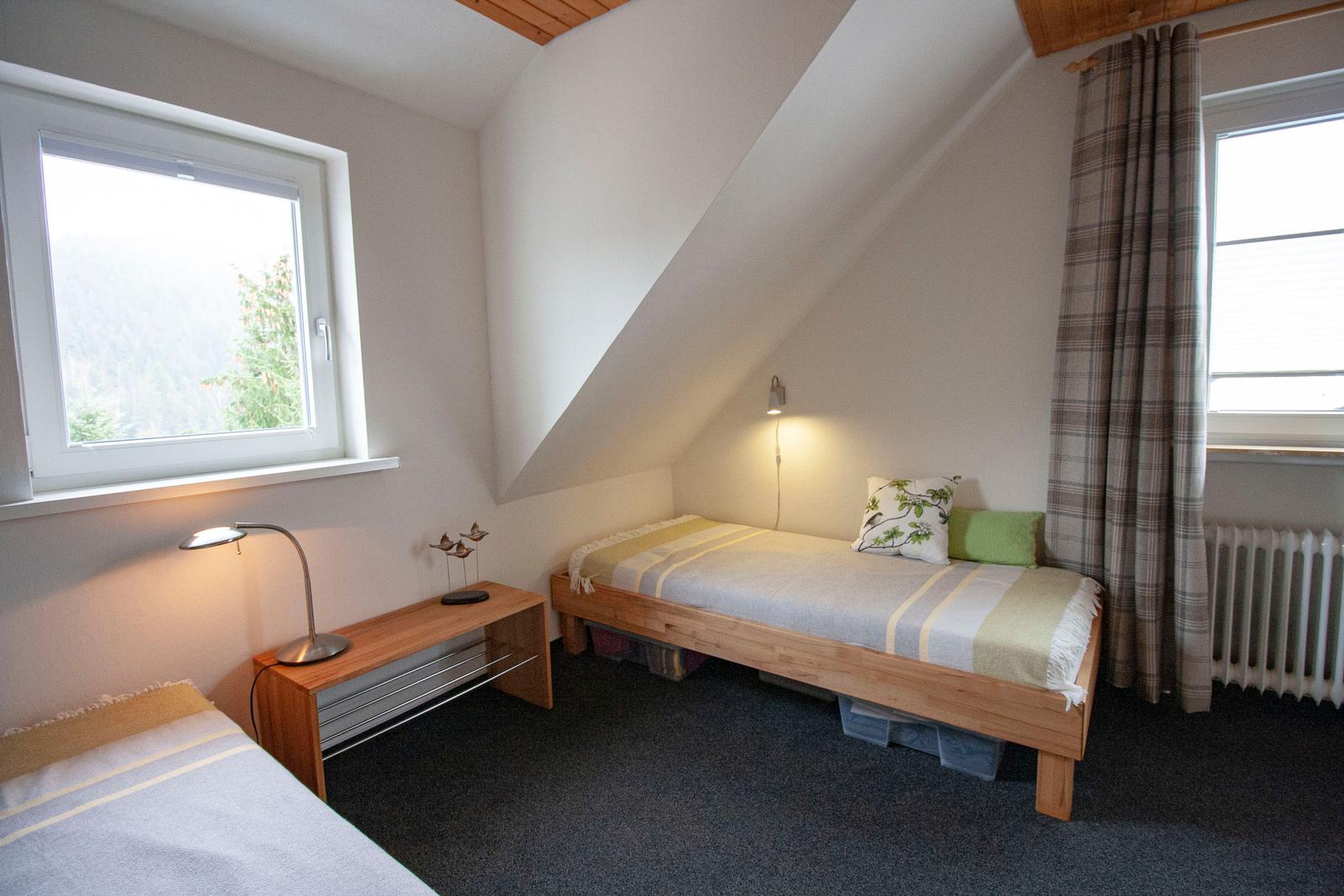 Zimmer mit zwei Betten, Fenstern und Dachschräge.