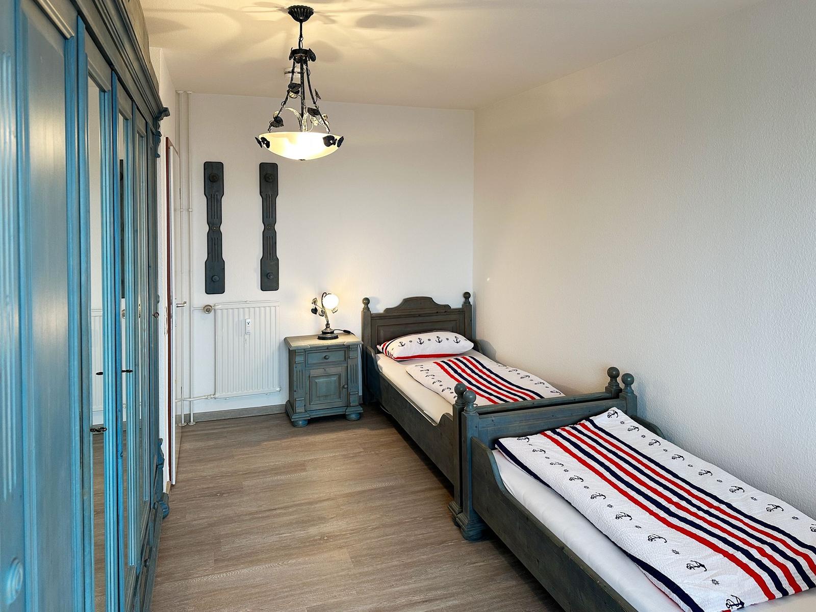 Zwei Betten mit Ankermotiv, blaues Schrank und Nachttisch, Deckenleuchte.