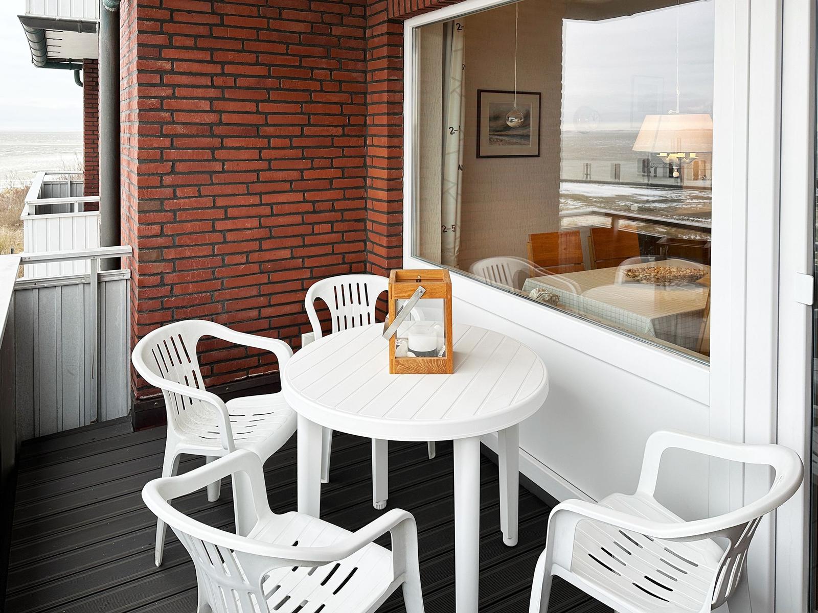 Terrasse mit weißem Tisch und Stühlen, roter Ziegelwand und Blick aufs Meer.