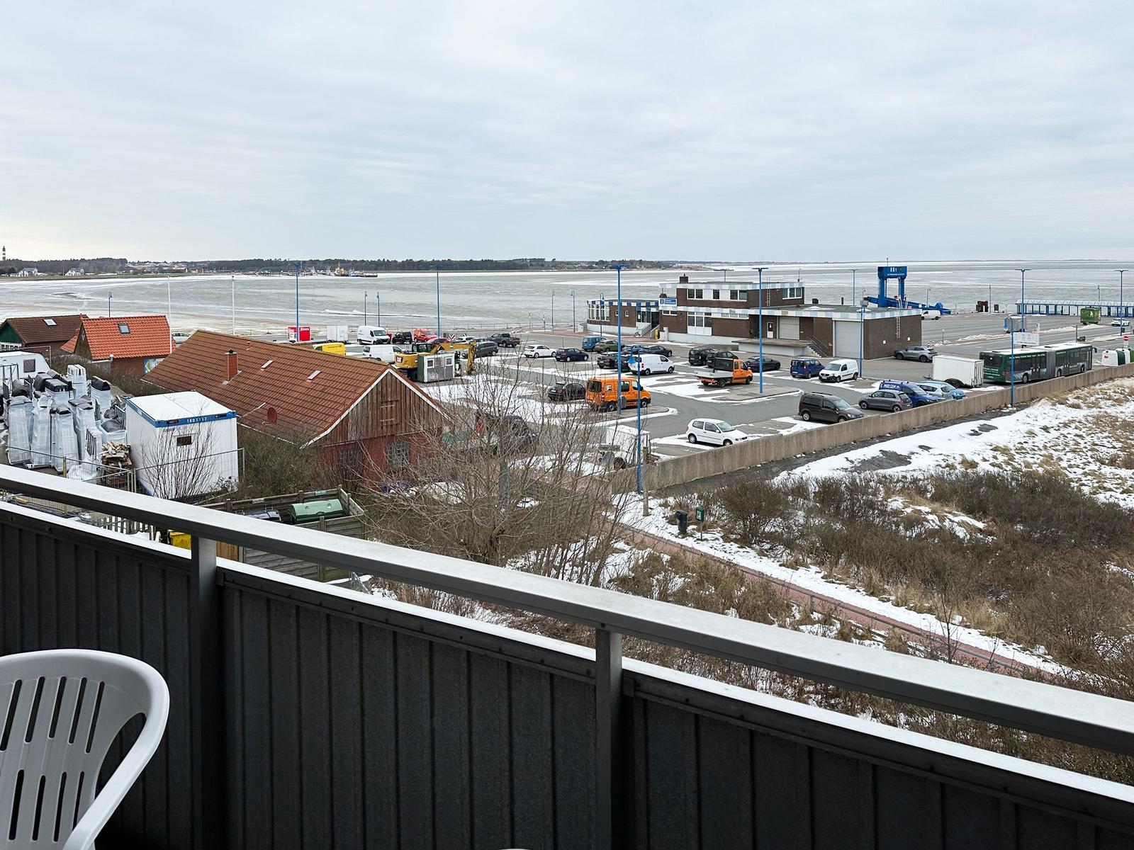 Blick vom Balkon auf Hafen, Parkplatz und Wasser mit Schneeflächen.