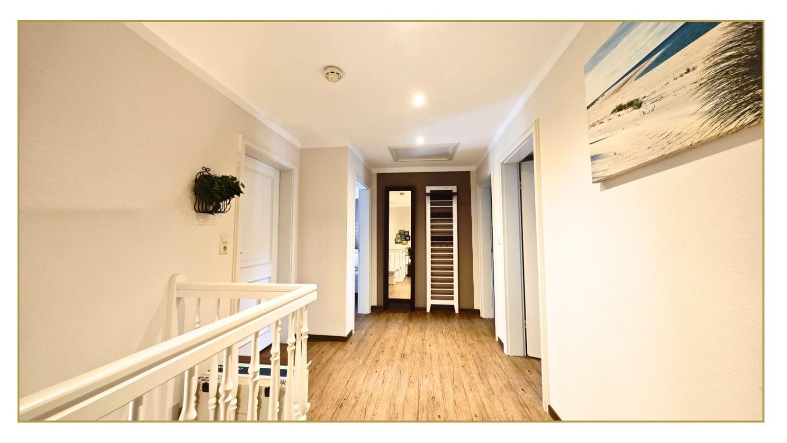 Hausflur mit Holzboden, weißen Türen und Wandbild. Treppenhaus links, Schrank rechts.