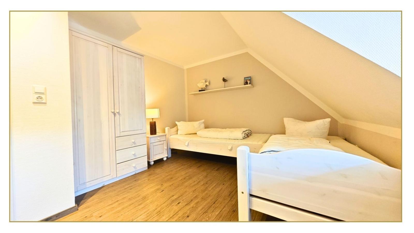 Zimmer mit zwei Betten, Kleiderschrank und Holzboden unter Dachschrägen.