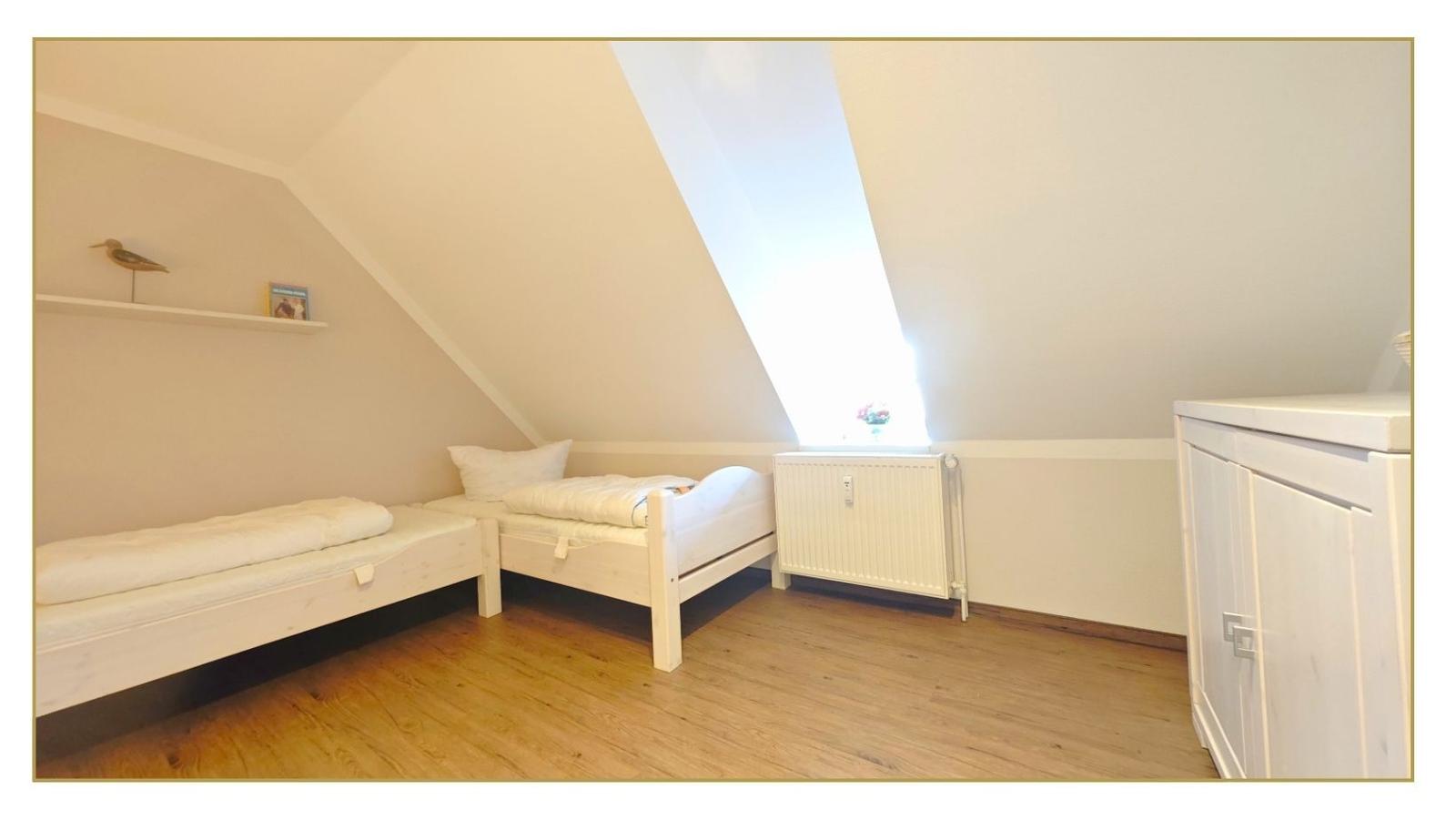 Zimmer mit zwei Betten, Dachschräge und Holzboden. Weiße Möbel und Heizung.