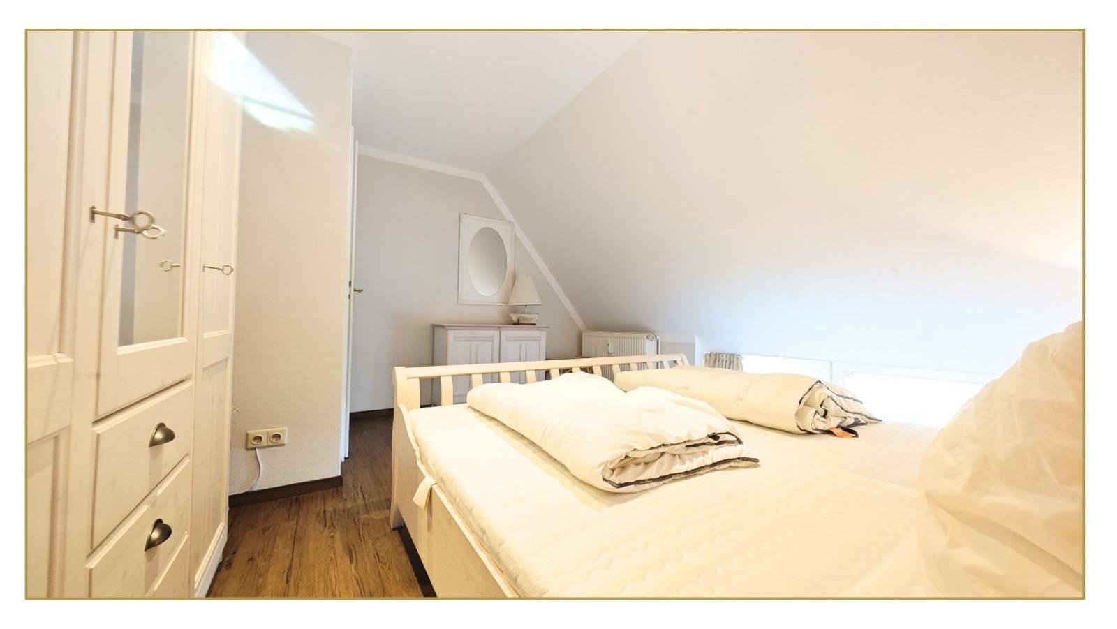 Schlafzimmer mit Dachschräge, Bett, Kleiderschrank und Spiegel.